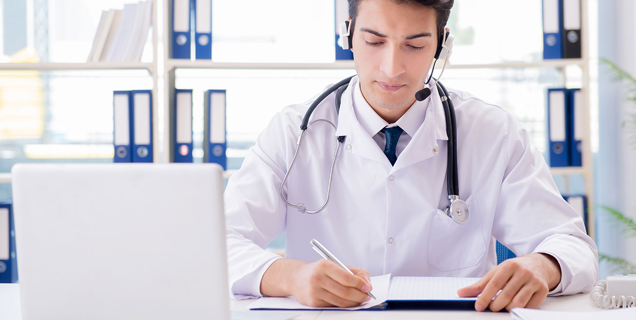 Médico jovem em consultório anotando em caderno o que escuta por telessaúde